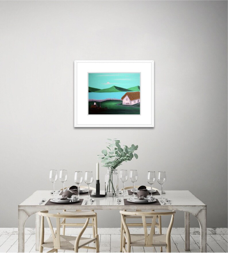 May include: A framed landscape painting featuring a white cottage with a brown roof, situated on a dark green field. In the background, a bright blue body of water is bordered by rolling green hills under a light blue sky.