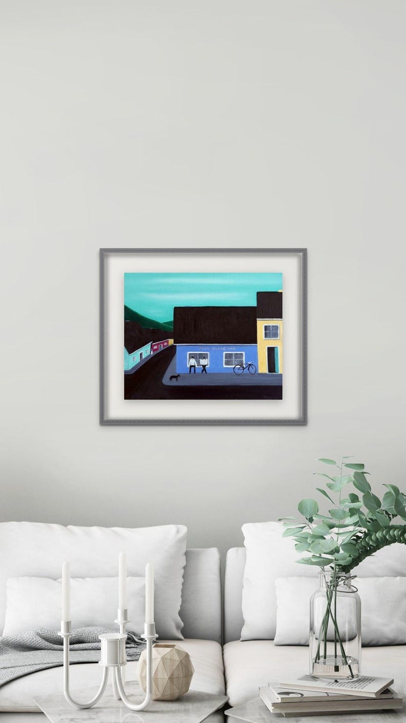 May include: A framed painting depicting a street scene with a blue building, a yellow building, and a dark roof. The blue building features two windows with figures inside, a bicycle parked outside, and a small black dog on the sidewalk.
