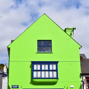 May include: A bright lime green building facade featuring a prominent blue bay window on the lower level and a single rectangular blue window above. A small blue street sign with white text reads Market Lane on the corner of the structure.
