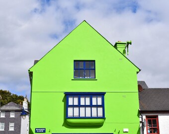 Könnte beinhalten: Eine leuchtend hellgrüne Gebäudefassade mit einem markanten blauen Erkerfenster im unteren Bereich und einem einzelnen rechteckigen blauen Fenster darüber. Ein kleines blaues Straßenschild mit weißer Aufschrift Market Lane ist angebracht.