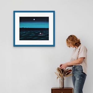 May include: A framed painting featuring a dark night scene with a bright white moon above a deep blue ocean. A small red boat with a white sail floats on the water. The artwork is enclosed in a white mat and a bold blue rectangular frame.