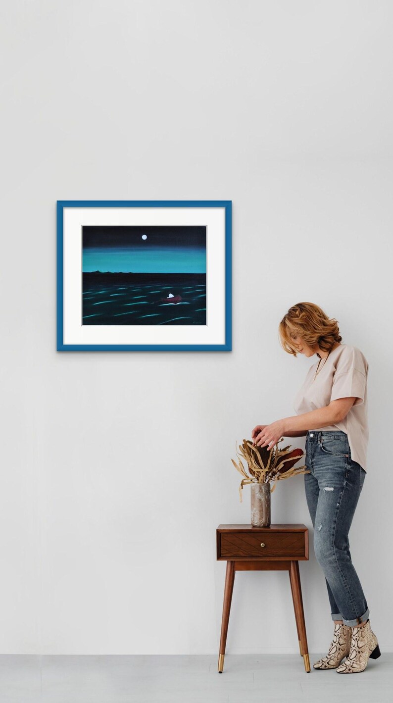 May include: A framed painting featuring a dark night scene with a bright white moon above a deep blue ocean. A small red boat with a white sail floats on the water. The artwork is enclosed in a white mat and a bold blue rectangular frame.