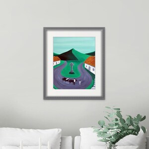 May include: A framed painting depicting a rural landscape with a winding purple road, two white cottages with orange roofs, a central stone cross, and a horse-drawn cart. The background features rolling green hills under a pale sky.