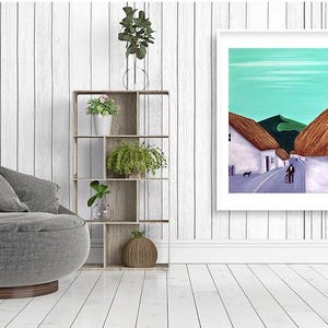 May include: A framed art print showing a village scene with white buildings, thatched roofs, and a road. The artwork features a teal sky and green hills. A grey chair, wooden shelf with plants, and a side table are also visible.