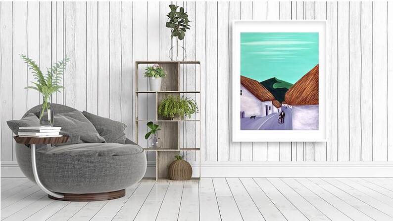 May include: A framed art print showing a village scene with white buildings, thatched roofs, and a road. The artwork features a teal sky and green hills. A grey chair, wooden shelf with plants, and a side table are also visible.