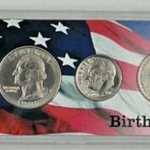 May include: A Birthyear Set of U.S. coins, including a half-dollar, quarter, dime, nickel, and penny, displayed in a clear plastic case. The background features an American flag design. The text "Birthyear Set" is visible.