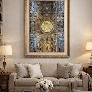 Könnte beinhalten: Ein gerahmter Druck einer detaillierten Decke mit goldenen und blauen Akzenten hängt über einem beigen Sofa. Das Kunstwerk zeigt ein kreisförmiges Design in der Mitte und ist von aufwendigen architektonischen Details umgeben. Der Raum umfasst einen Couchtisch, Lampen und eine neutrale Farbpalette.