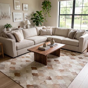 Puede incluir: Una alfombra grande con un patrón repetitivo de formas festoneadas en tonos beige, crema y marrón. La alfombra está hecha de piezas individuales de piel con una textura suave, cubriendo un suelo de madera clara bajo una mesa de centro de madera.