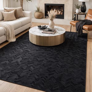 Könnte beinhalten: Ein großer, rechteckiger schwarzer Teppich mit Fischgrätmuster. Der Teppich liegt auf einem Holzboden in einem Wohnzimmer, mit einem Sofa, einem Couchtisch und einem Kamin im Hintergrund.