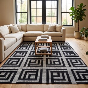 May include: A rectangular area rug featuring a repeating geometric pattern of black and grey concentric squares. The design consists of bold black lines forming nested right-angle shapes against a textured grey background, covering the floor.