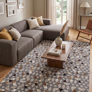 May include: A large rectangular area rug featuring a repeating geometric pattern of triangles in shades of grey, white, brown, and black. The rug is constructed from individual patches, creating a textured surface that covers the wooden floor.