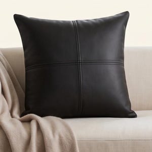 Peut inclure: Un coussin carré de couleur noir charbon foncé uni. Le coussin présente un motif de couture distinct en forme de croix qui traverse verticalement et horizontalement le centre, créant quatre quadrants égaux sur la surface avant.