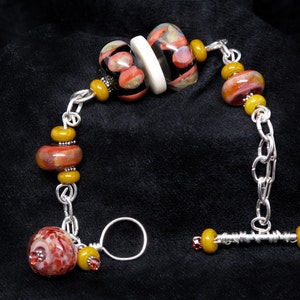 May include: A silver chain bracelet with a toggle clasp. The bracelet features a variety of colorful glass beads, including black, red, and yellow.