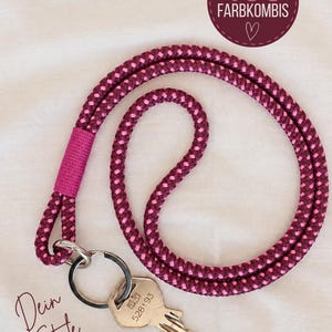 Könnte beinhalten: Ein Schlüsselband aus geflochtenem Seil in Dunkelmagenta und Hellrosa mit einem einfarbig rosa umwickelten Abschnitt, einem silbernen Metallring und einem silbernen Schlüssel. Der Text auf dem Bild lautet FAST 400 FARBKOMBIS und Dein Style.