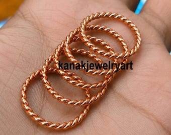 Peut inclure: Un ensemble de cinq bagues de couleur cuivre, chacune présentant une texture torsadée semblable à une corde. Les bagues sont empilées en se chevauchant légèrement. Le texte "kanakjewelryart" est imprimé en noir au centre des bagues.