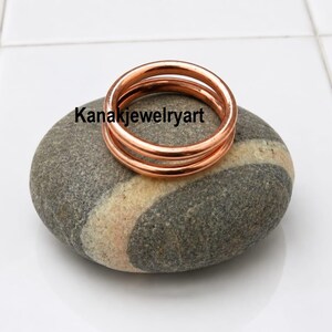 May include: A polished copper ring with a smooth, rounded band design. The ring features a double-layered appearance and is marked with the text Kanakjewelryart. The metal has a warm, metallic orange-brown hue and a reflective surface finish.