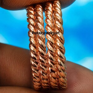 Könnte beinhalten: Ein Set aus drei kupferfarbenen Ringen mit gedrehter Seilstruktur. Die Ringe haben eine polierte, metallische Oberfläche und sind übereinander gestapelt. Der Text "kanakjewelryart" ist in Schwarz über die Ringmitte gedruckt.