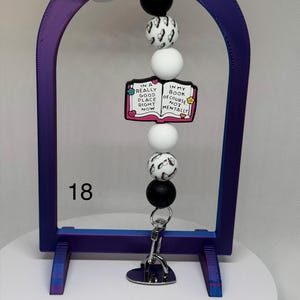 May include: A beaded keychain with a book-themed charm. The charm reads "In a really good place right now, in my book of course not mentally." The keychain features black, white, and patterned beads, and a silver-tone clip.
