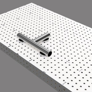 May include: A large, white metal welding table with a perforated surface and two silver metal tubes. The table has four legs, with wheels on two of them. The wheels are attached to yellow supports.