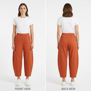 Op de afbeelding: Voor- en achteraanzicht van een vrouw in een wit T-shirt en een roestkleurige broek met wijde pijpen. De broek heeft een tailleband met trekkoord en zakken. De outfit is eenvoudig en casual.