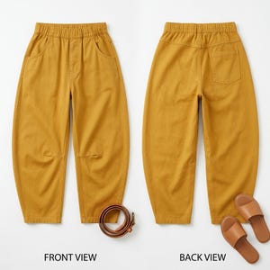 Op de afbeelding: Mosterdkleurige broek met een elastische tailleband, voorzakken en een enkele achterzak. De voorkant toont de broek met een bruine riem, terwijl de achterkant wordt getoond met bruine sandalen. De broek heeft een relaxte pasvorm.