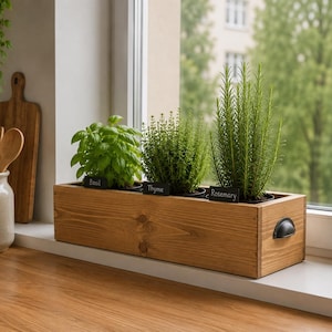 May include: A rectangular wooden planter box with a natural grain finish and black metal side handles. It contains three potted herbs, each with a small black rectangular label reading Basil, Thyme, and Rosemary, arranged in a row.