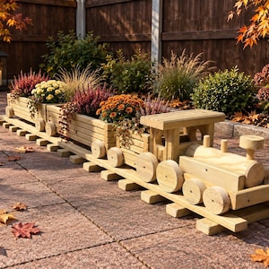 May include: A wooden train planter set consisting of a locomotive engine and two connected cargo cars, all featuring circular wheels and slatted sides. The train sits on a wooden track base, with the cargo cars filled with colourful autumn flowers.