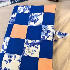 Peut inclure: Une housse en tissu rectangulaire présentant un motif patchwork composé de carrés bleu roi unis, de carrés pêche unis et de carrés blancs à motif floral bleu. Une petite étiquette blanche avec le texte Willow & Fern est cousue sur le devant.