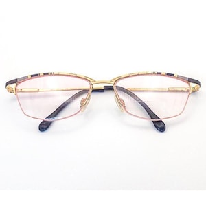 May include: Gold-rimmed eyeglasses with a rectangular shape and a black nose bridge. The frames have a decorative pattern on the top and are set against a white background. The lenses are a light pink color.