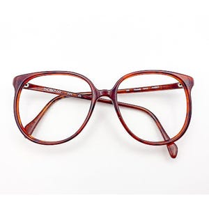 May include: Brown tortoiseshell eyeglasses with a rounded square frame. The glasses have a classic design with a keyhole bridge and thin temples. The lenses are clear, and the frame is a warm, reddish-brown color.