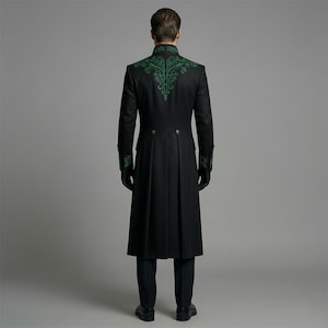May include: A long black coat with green embroidered detailing on the shoulders and cuffs. The coat has a high collar and a button closure. The person is wearing black gloves and black pants. The coat is a formal style.