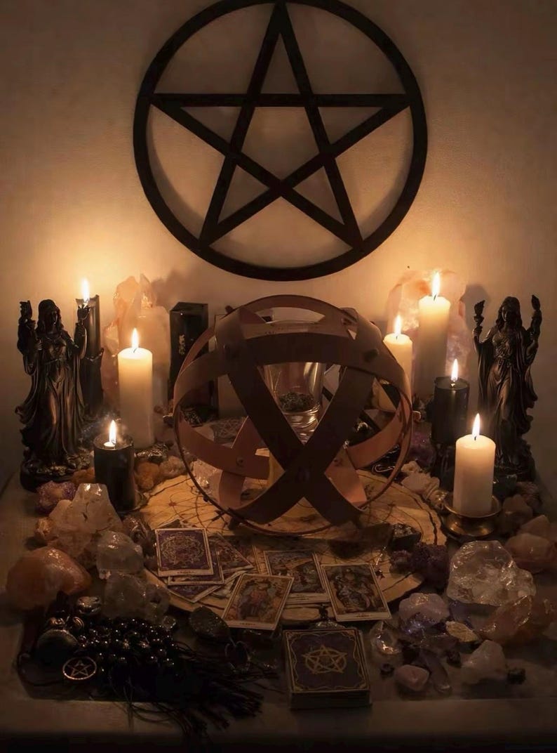 Puede incluir: Un altar m&iacute;stico con un pentagrama, velas, cristales, cartas del tarot y una esfera met&aacute;lica decorativa. Dos estatuas flanquean las velas. La escena est&aacute; iluminada con una luz c&aacute;lida.