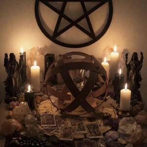 Pu&ograve; includere: Un allestimento con un grande pentagramma nero a parete sopra candele bianche e nere, due statue scure, vari cristalli, carte dei tarocchi e una struttura sferica in legno al centro su un tappetino circolare.