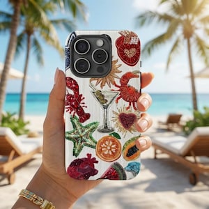 May include: A white phone case featuring embroidered motifs such as a lobster, starfish, and martini glass. The case has a wood grain effect and is held against a beach scene with palm trees and the sea.