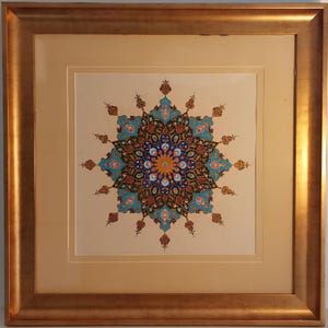 May include: A framed artwork featuring a symmetrical, colorful design. The central motif is a circular pattern with blue, orange, and brown elements. The artwork is set against a cream-colored background and framed in a gold-toned wooden frame.