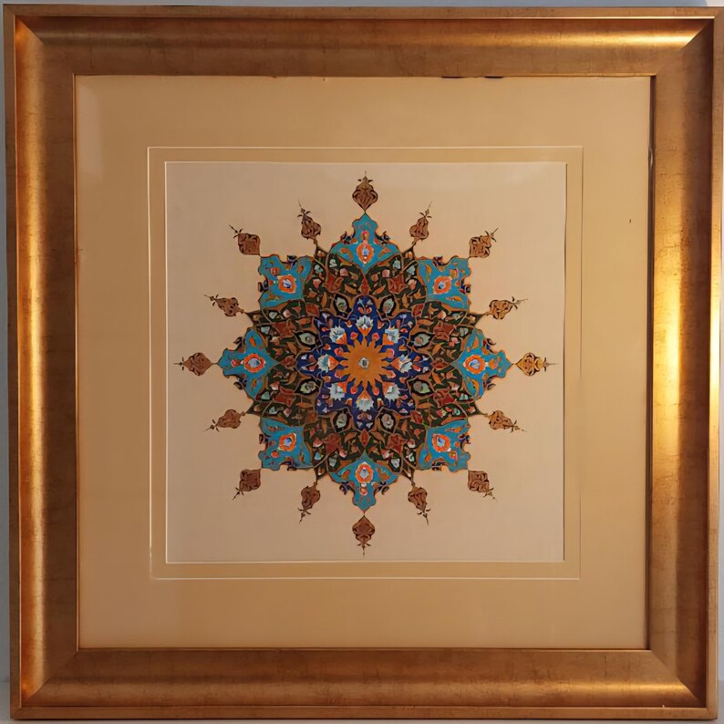 May include: A framed artwork featuring a symmetrical, colorful design. The central motif is a circular pattern with blue, orange, and brown elements. The artwork is set against a cream-colored background and framed in a gold-toned wooden frame.