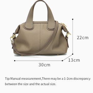 May include: A taupe-colored handbag with a top handle and a detachable shoulder strap. The bag is 30 cm long, 22 cm high, and 13 cm wide. It features gold-colored hardware and a zipper closure. The bag's measurements may vary slightly.