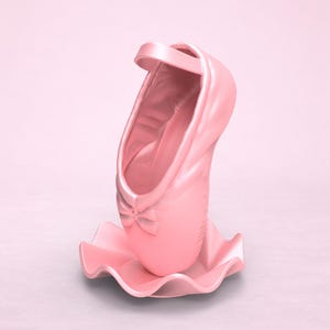May include: A light pink ballet slipper sculpture standing upright on a matching wavy, circular base. The shoe features a small decorative bow at the toe and a single strap across the top opening, all rendered in a smooth, solid matte finish.