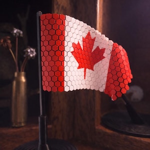 May include: A decorative Canadian flag, with a red maple leaf on a white background, made from red and white hexagonal tiles. The flag is mounted on a black stand with a circular base. A patriotic item.
