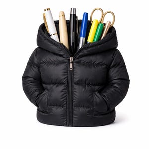Puede incluir: Un organizador de escritorio negro con forma de chaqueta acolchada, con capucha y cremallera. La chaqueta está llena de bolígrafos, tijeras y otros útiles de oficina. El organizador tiene dos bolsillos y está sobre un fondo blanco.