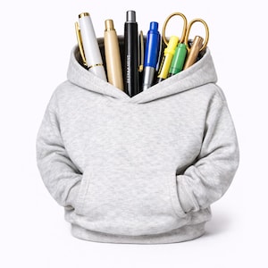 May include: A light gray hoodie filled with various pens, pencils, and a pair of gold scissors. The pens are white, black, blue, yellow, and green. The hoodie has a front pocket and a hood.