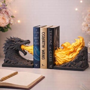 May include: A pair of black dragon bookends featuring a sculpted dragon head breathing a bright yellow flame on one side and a matching yellow flame emerging from a rocky base on the other, supporting three hardcover books standing upright.
