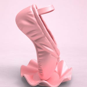 May include: A light pink ballet slipper sculpture standing upright on a matching pink, circular, ruffled base. The shoe features a smooth, matte finish with a single strap across the top opening, presented in a monochromatic design.