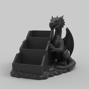 Pode incluir: Um organizador de mesa preto com tema de drag&atilde;o com tr&ecirc;s compartimentos em camadas. O drag&atilde;o tem olhos vermelhos e est&aacute; posicionado ao lado do organizador. O organizador &eacute; feito de um material escuro e assenta sobre uma base texturizada.