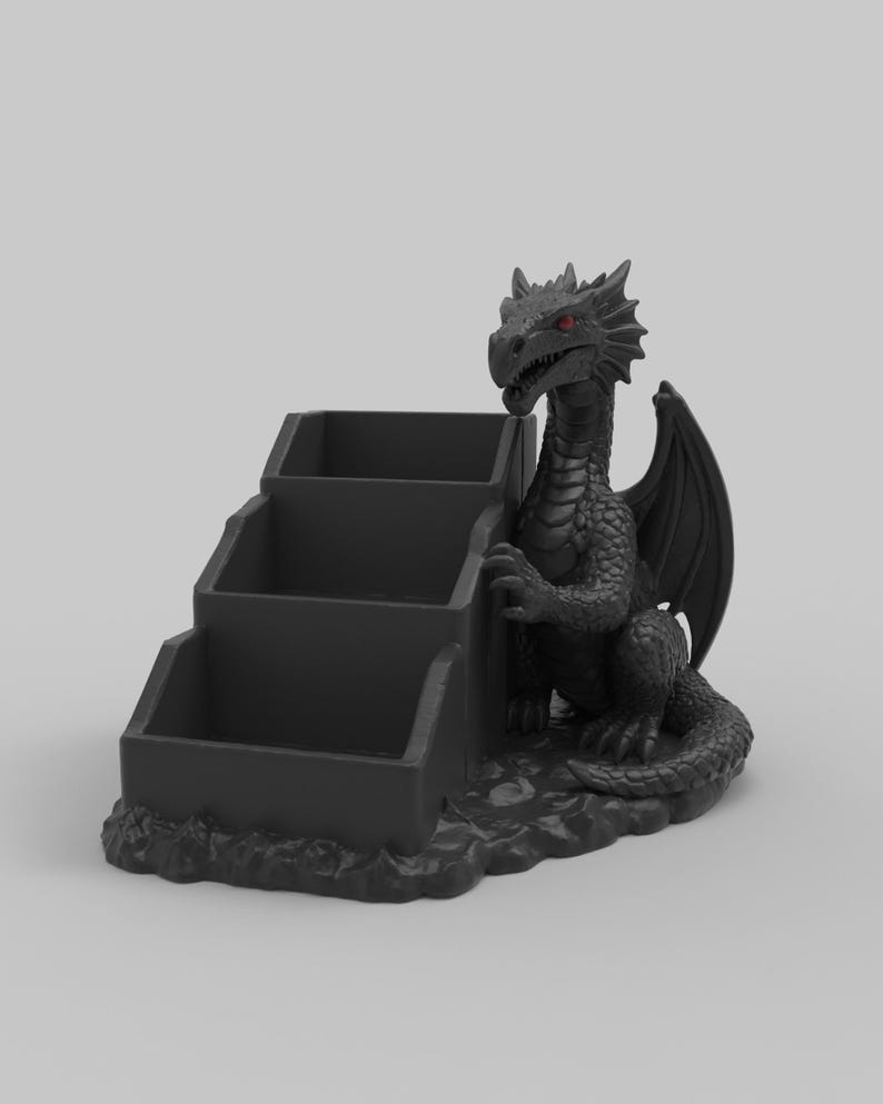 Pode incluir: Um organizador de mesa preto com tema de drag&atilde;o com tr&ecirc;s compartimentos em camadas. O drag&atilde;o tem olhos vermelhos e est&aacute; posicionado ao lado do organizador. O organizador &eacute; feito de um material escuro e assenta sobre uma base texturizada.