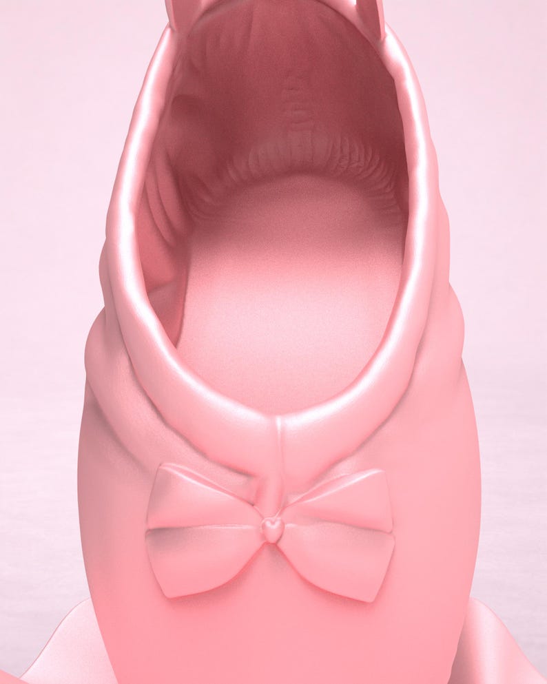 May include: A light pink ballet slipper featuring a smooth, matte finish and a decorative bow centered at the front. The shoe has a rounded opening and a structured design, showcasing a uniform pastel pink color throughout the entire exterior surface.