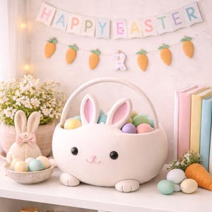 May include: A white Easter bunny-shaped basket filled with pastel eggs. The basket has pink-lined ears and a cute face. A banner reading "HAPPY EASTER" hangs above, with carrot decorations. A plush bunny and a bowl of eggs are also on display, creating an Easter theme.