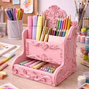 Puede incluir: Un organizador de escritorio rosa y ornamentado lleno de bolígrafos, lápices y rotuladores de colores. El organizador tiene múltiples compartimentos y adornos decorativos. Una variedad de materiales de arte son visibles en el escritorio, incluyendo pintura y papel.