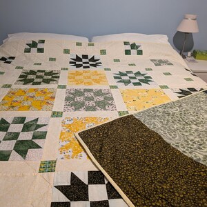 May include: A patchwork quilt with a variety of patterns and colours. The quilt features star and floral motifs in green, yellow, black, and white squares. The quilt is on a bed with white pillows. The quilt is handmade.