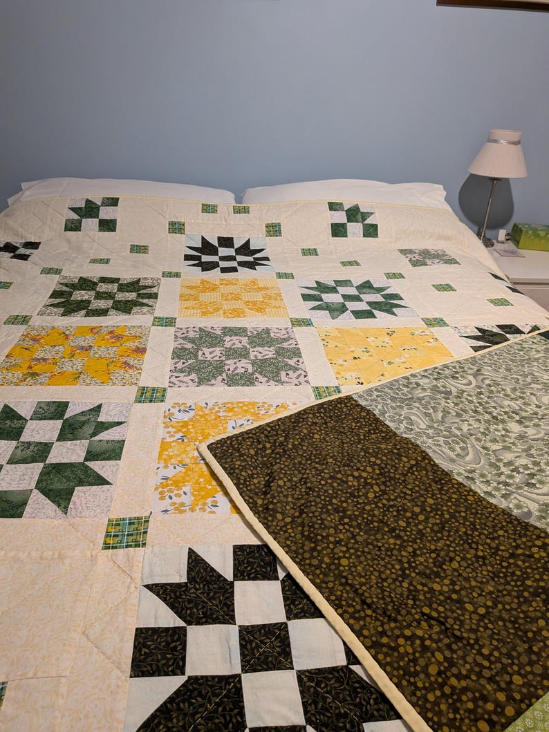 May include: A patchwork quilt with a variety of patterns and colours. The quilt features star and floral motifs in green, yellow, black, and white squares. The quilt is on a bed with white pillows. The quilt is handmade.